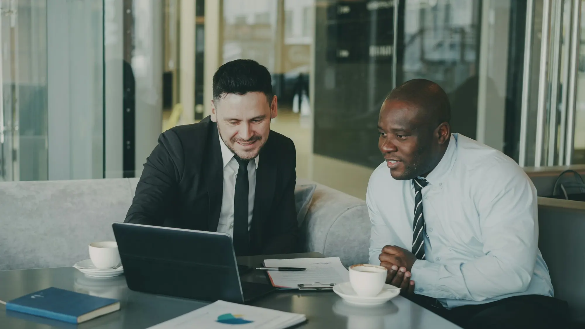 Two executives, one white and one Black, reviewing work together on a laptop